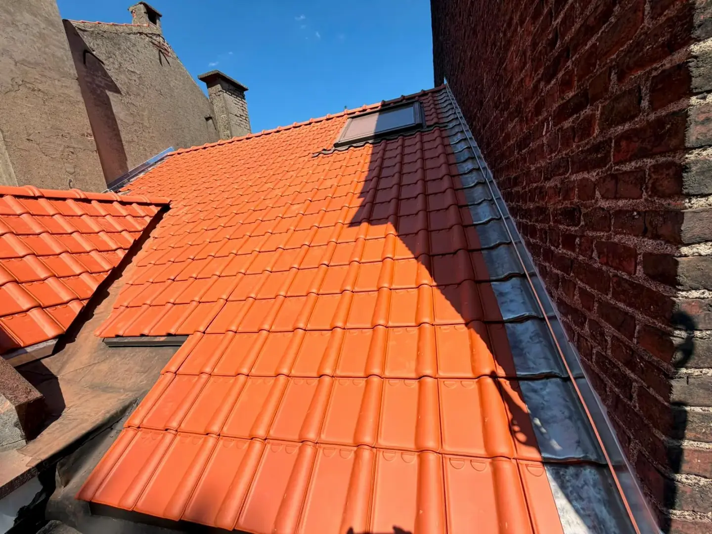 Versant neuf en tuiles rouges avec fenêtre de toit, raccordé au mur mitoyen par un solin en zinc